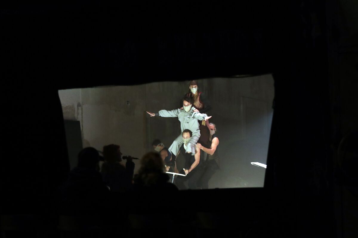 Spectators enjoy a performance through a window at a theater in Prague, Czech Republic, Tuesday, Nov. 10, 2020. Desperate to play for at least some spectators amid the coronavirus pandemic, a new circus company Cirk La Putyka has started to play five-minutes performances on a stage behind a window. With all theaters closed due to the government restrictive measures, the theater adopted the same principle as the restaurants closed for the same reason. (AP Photo/Petr David Josek)