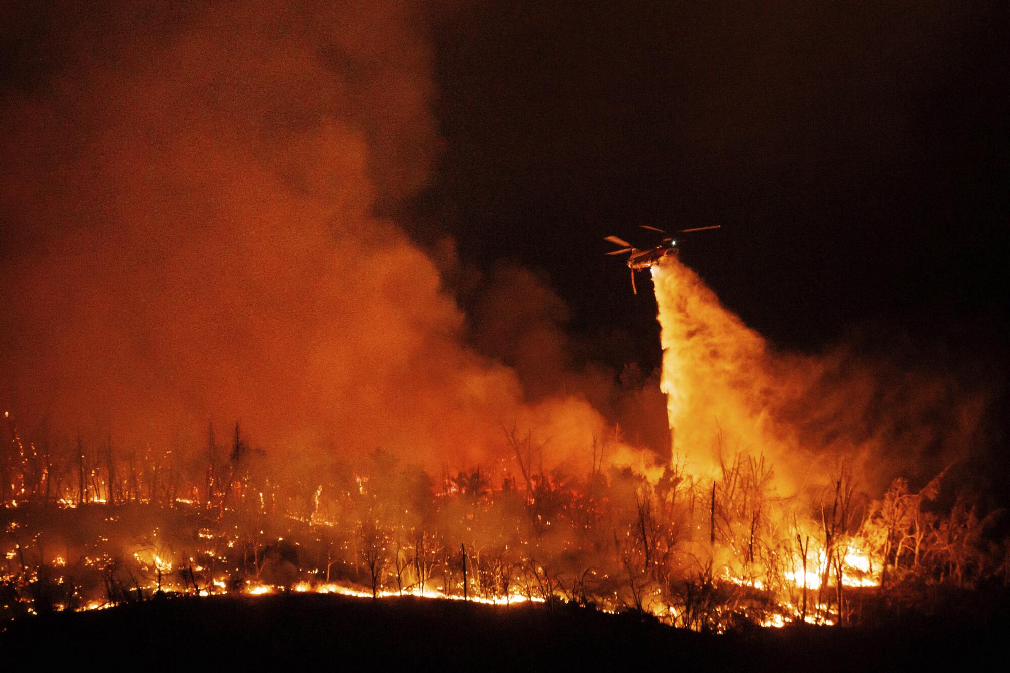 A helicopter drops water on flames at night.