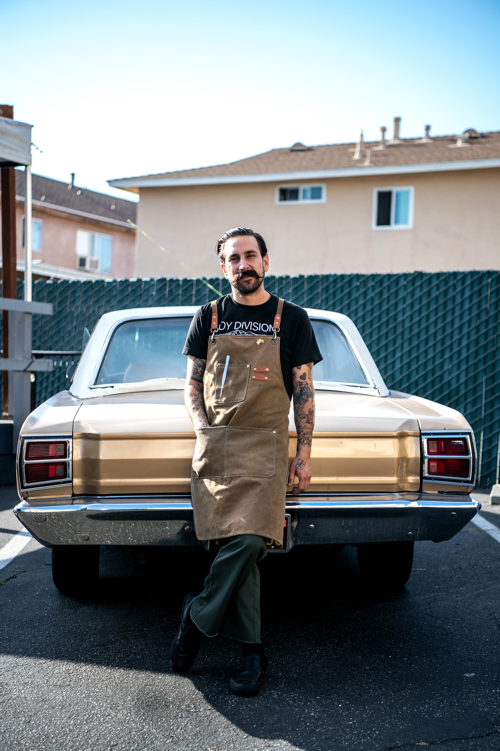 A man in an apron stands in front of a car.