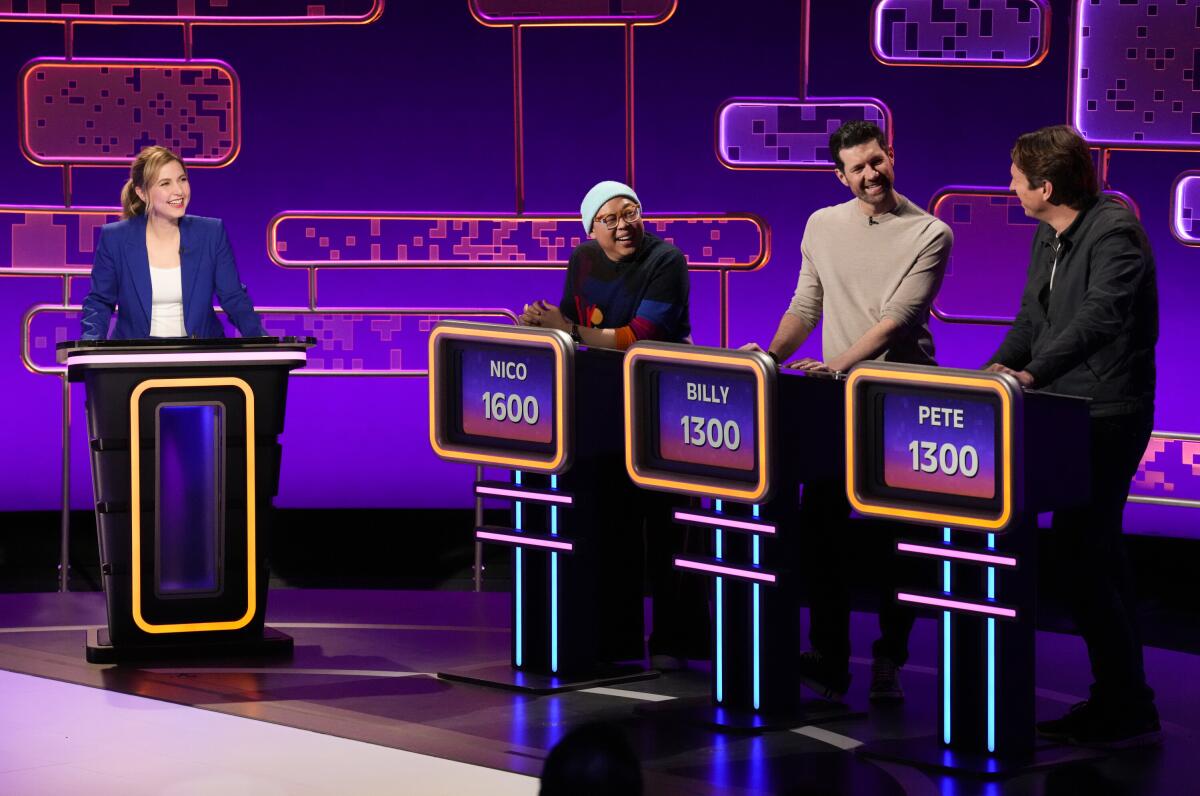 A game show host stands behind a podium and watches three contestants.