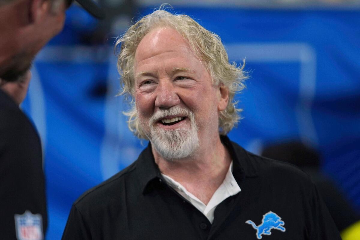 Timothy Busfield in a black sports shirt smiling against a blue backdrop.