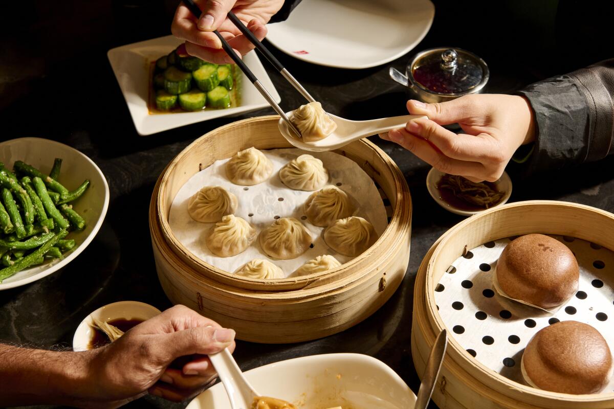 A spread of food at a table at Din Tai Fung,  including xiao long bao, green beans, steamed buns and cucumbers.