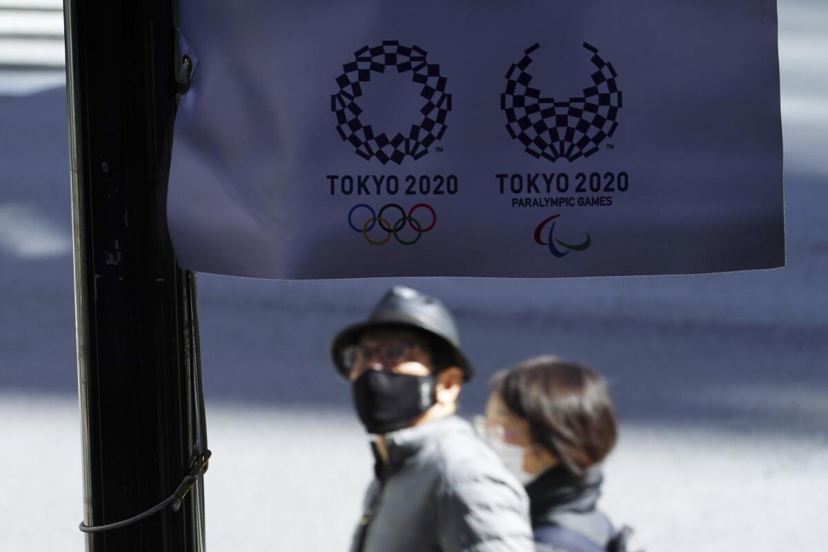 People wearing protective masks to help curb the spread of the coronavirus walk near a banner of Tokyo 2020 Olympic and Paralympic Games Wednesday, March 3, 2021, in Tokyo. The Japanese capital confirmed more than 310 new coronavirus cases on Wednesday. (AP Photo/Eugene Hoshiko)