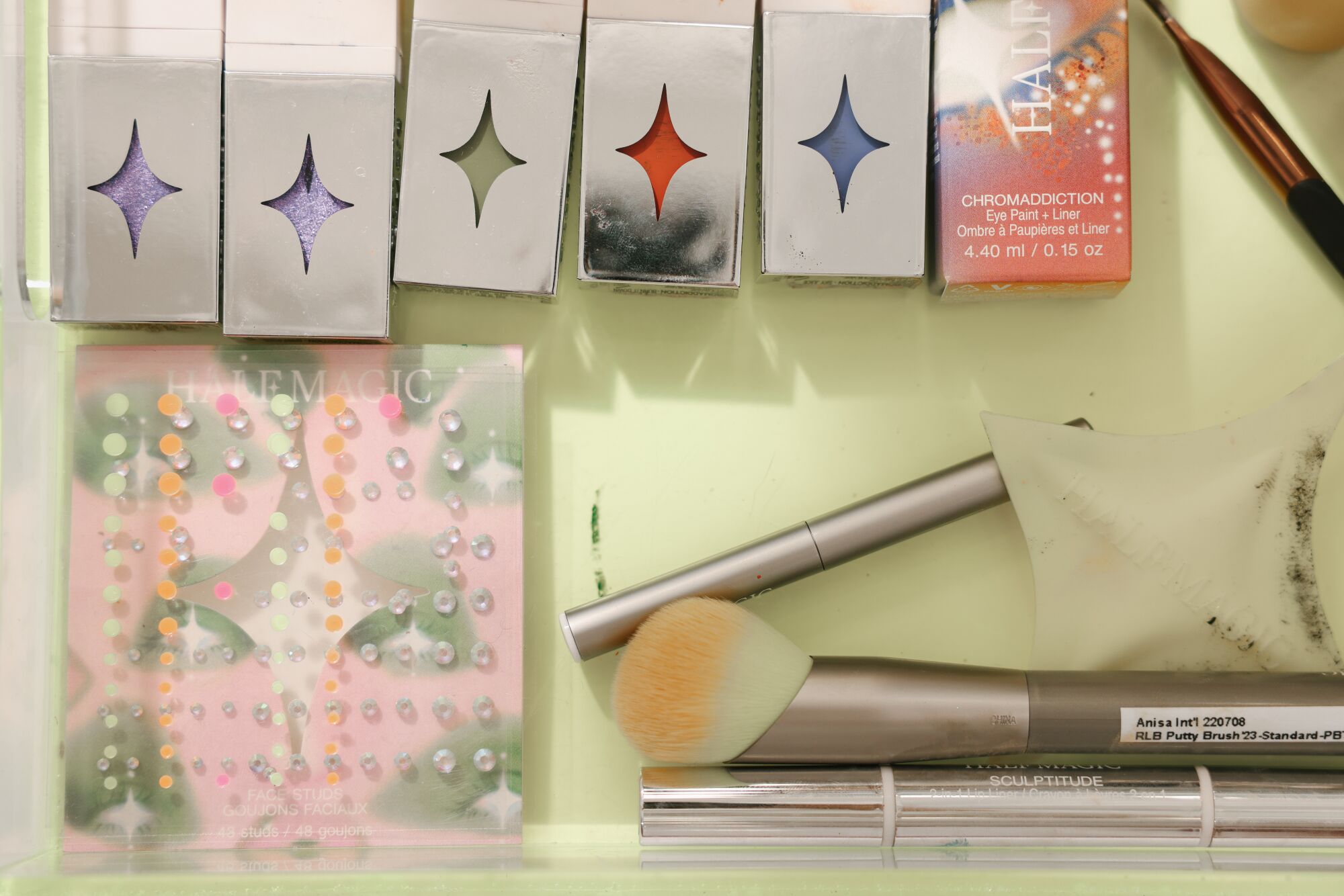 Brushes, rhinestones and pigmented makeup in a light green box.