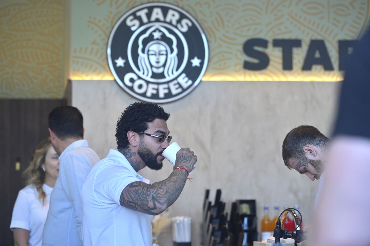 A tattooed man drinks coffee under a Stars Coffee logo