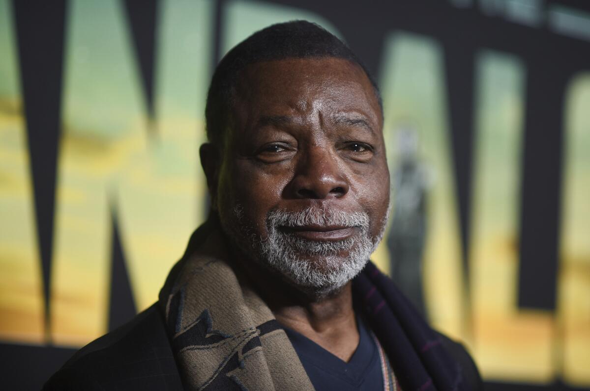 Carl Weathers, with a white goatee and a scarf, looks straight into the camera. 