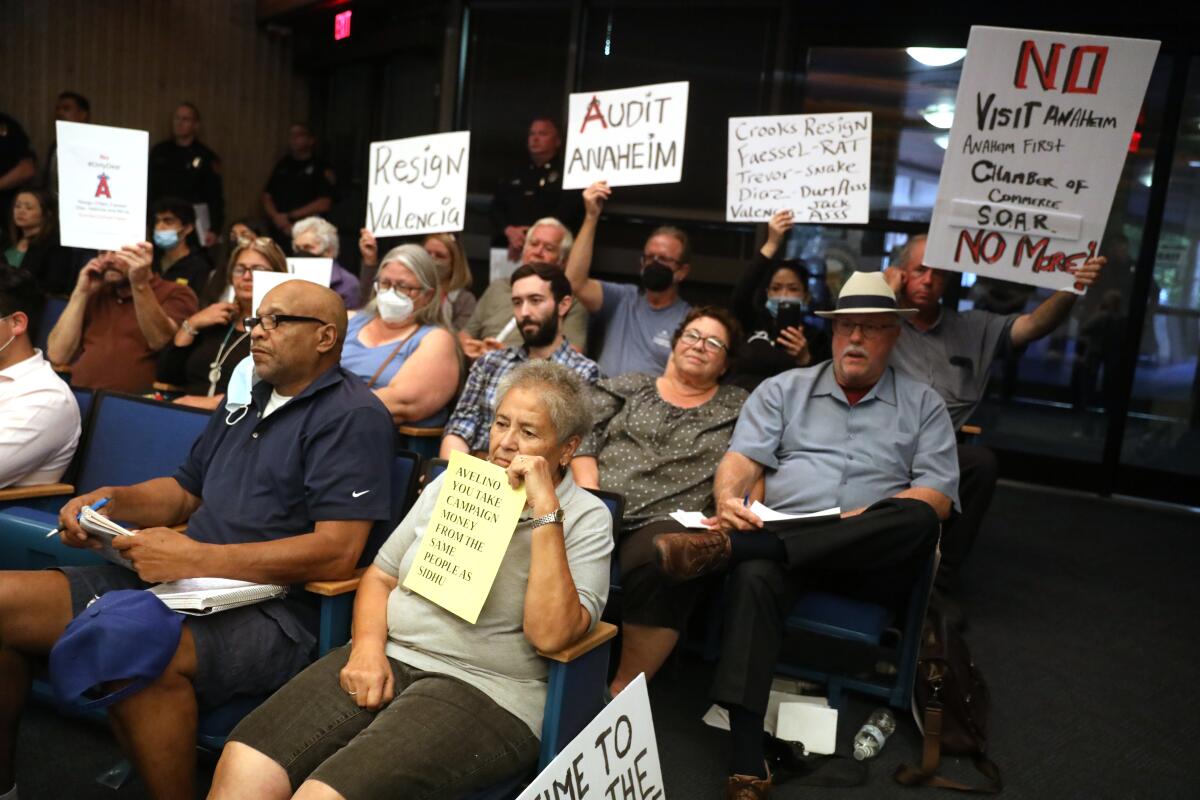 People hold signs as they watch a council meeting.