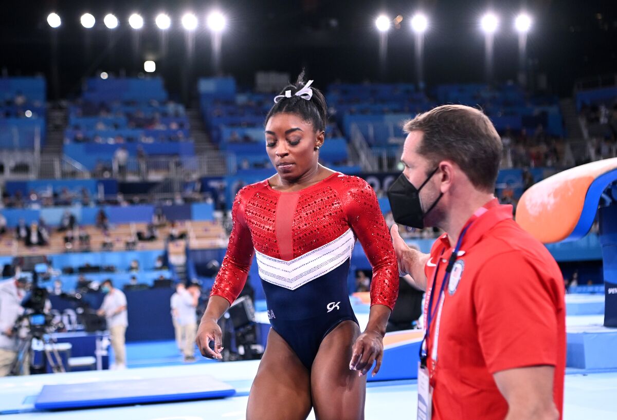 A man in a mask helps Simone Biles off the floor during the Tokyo Olympics.