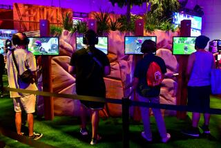 Four young men wearing headphones stand in front of four different screens playing a video game in a convention center