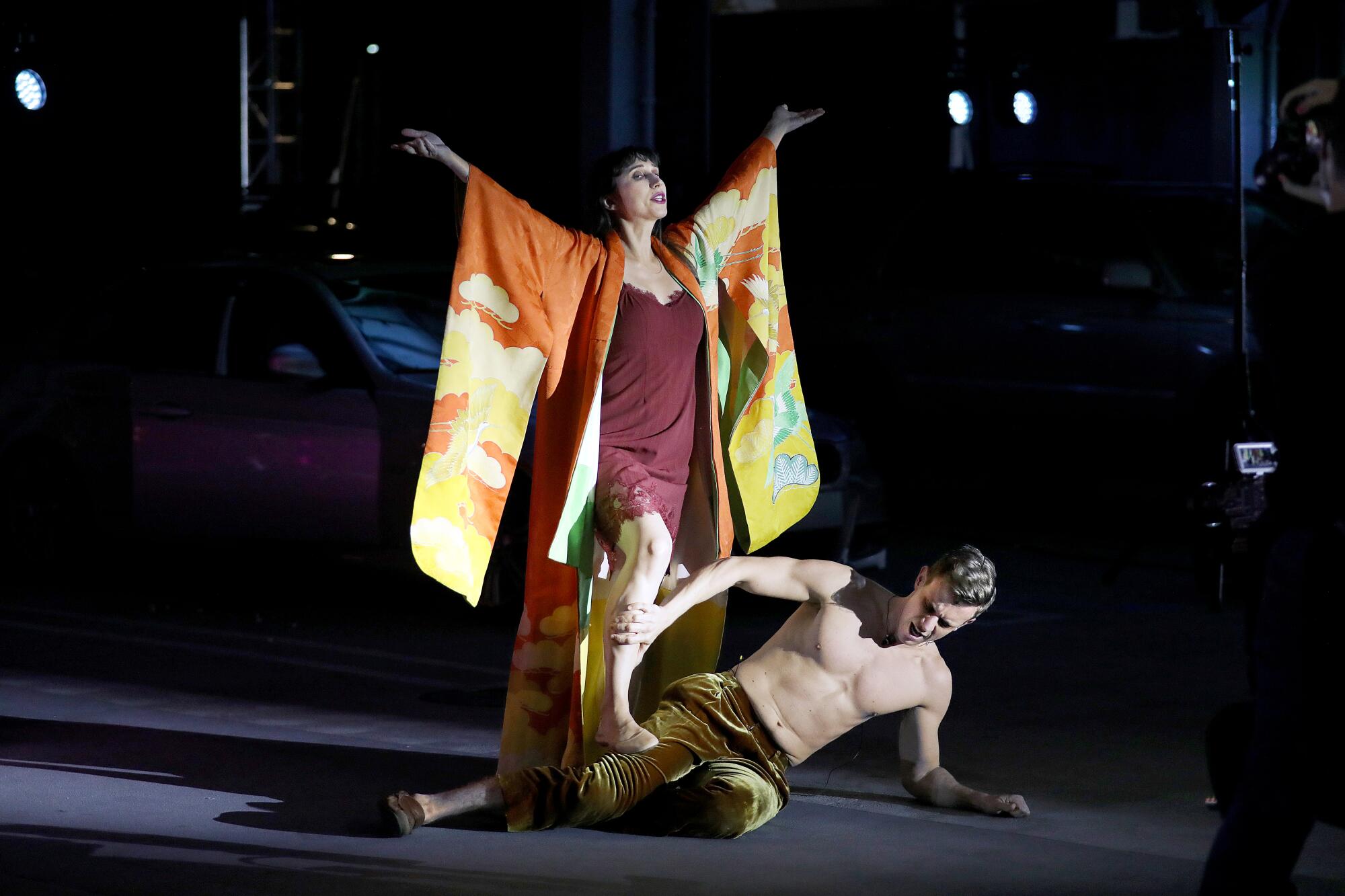 A woman with her arms outstretched stands over a man on the floor.