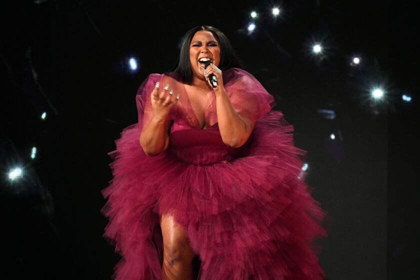 A woman performing in a magenta tulle gown sings into a microphone