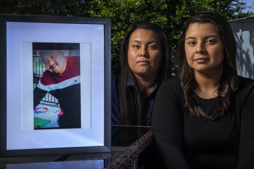NORWALK, CA-MAY 27, 2022: Johanna Garcia, 27, left, and her sister Katherine Garcia, 21, are photographed at their home in Norwalk. They are the daughters of Enrique Garcia, seen in framed photograph, a 49 year old Santa Ana man and forklift operator who died in December of 2017 after a medical procedure at South Coast Global Medical Center. The Garcia sisters sued a gastroenterologist for negligence but lost at trial last moth on Orange County civil court. After the verdict, Robert McKenna III, an attorney representing the doctor, appeared in a social-media post celebrating the verdict in a way that sparked controversy. (Mel Melcon / Los Angeles Times)