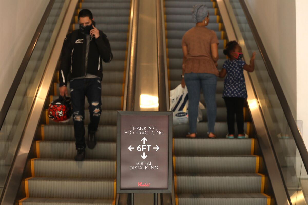A sign in front of an escalator reminds shoppers to keep six feet apart