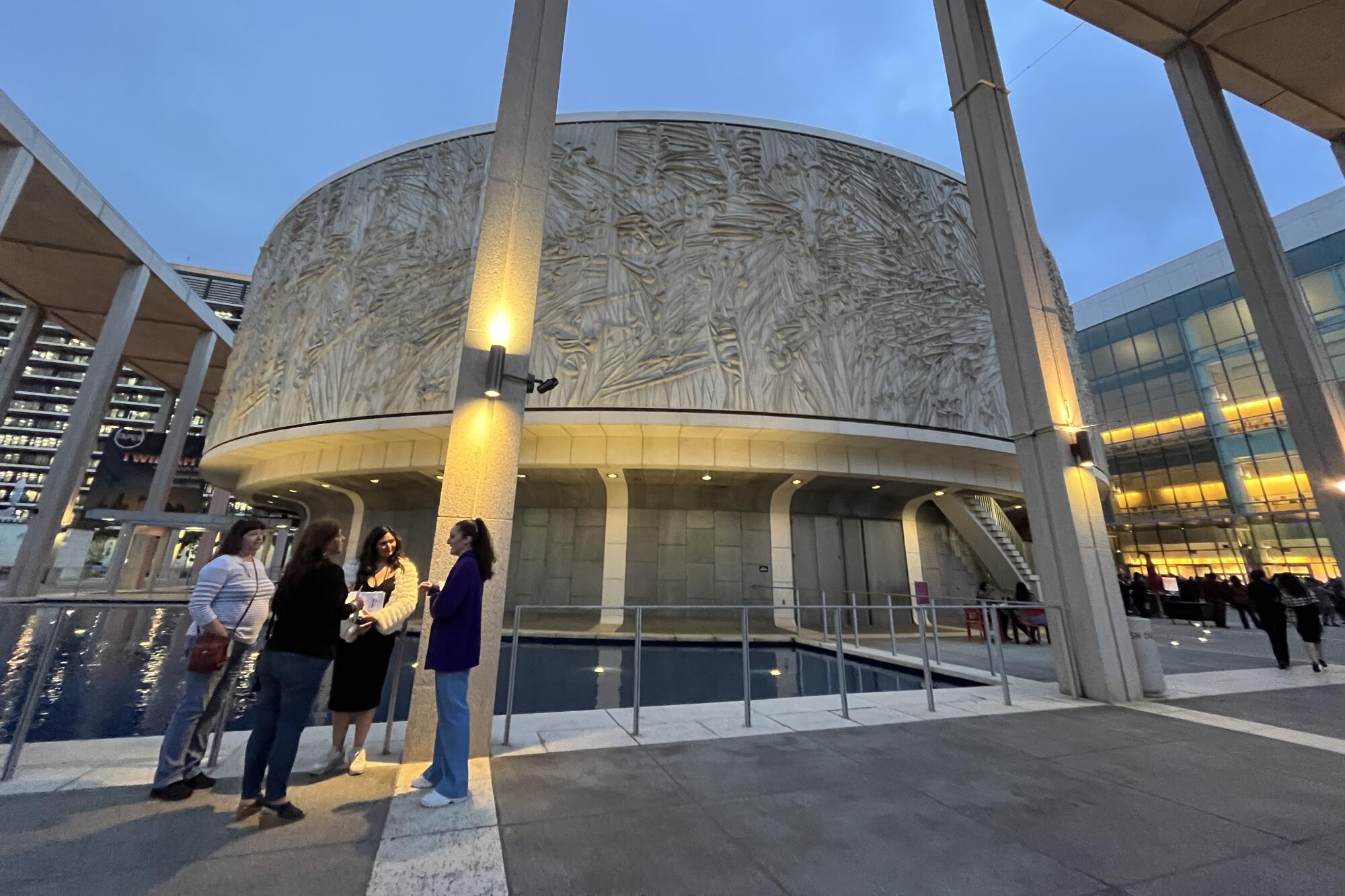 Four women stand outside the Mark Taper Forum, lighted up at twilight.