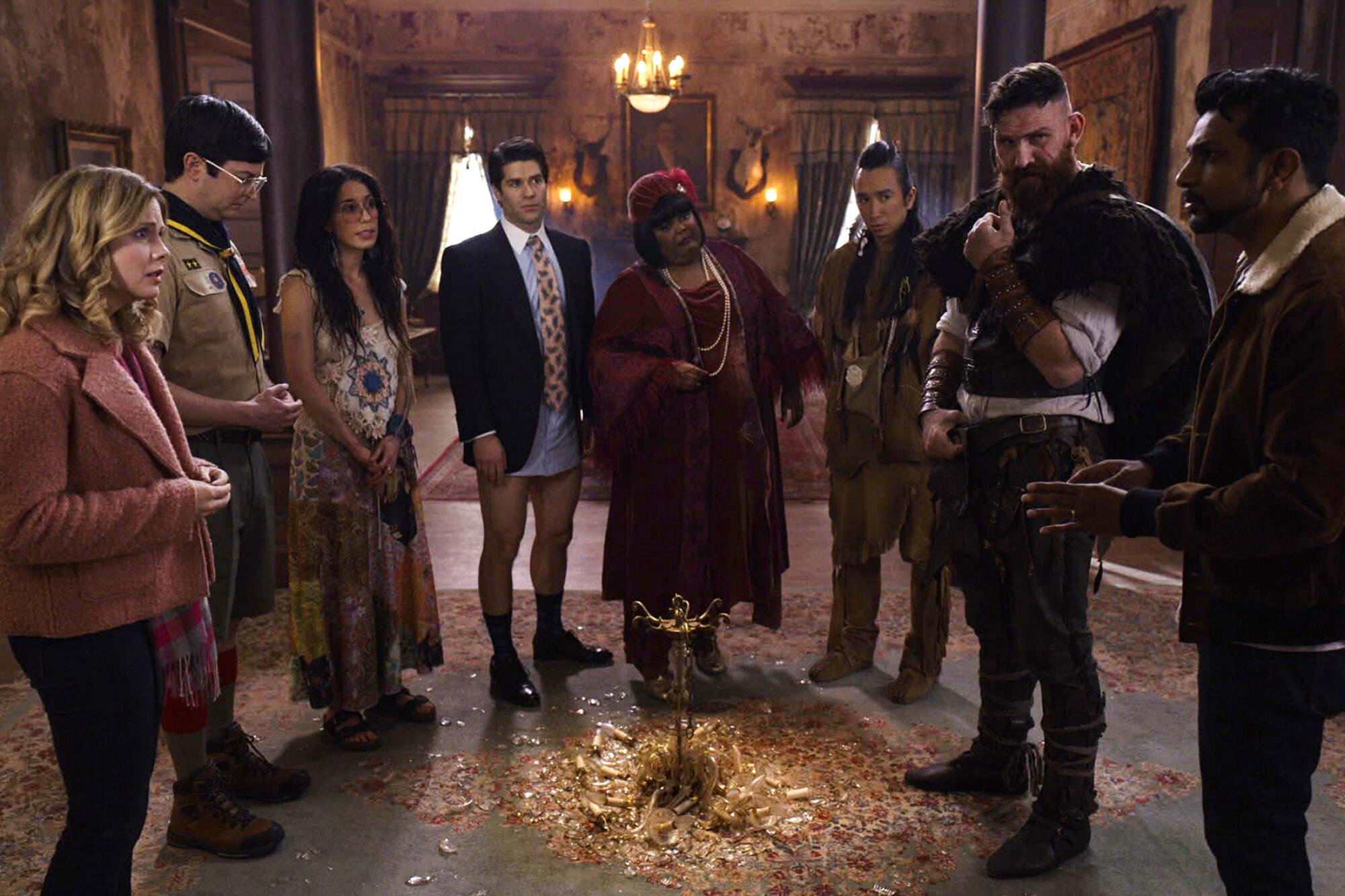 Eight people stand in a semi circle around a shattered chandelier on the floor.