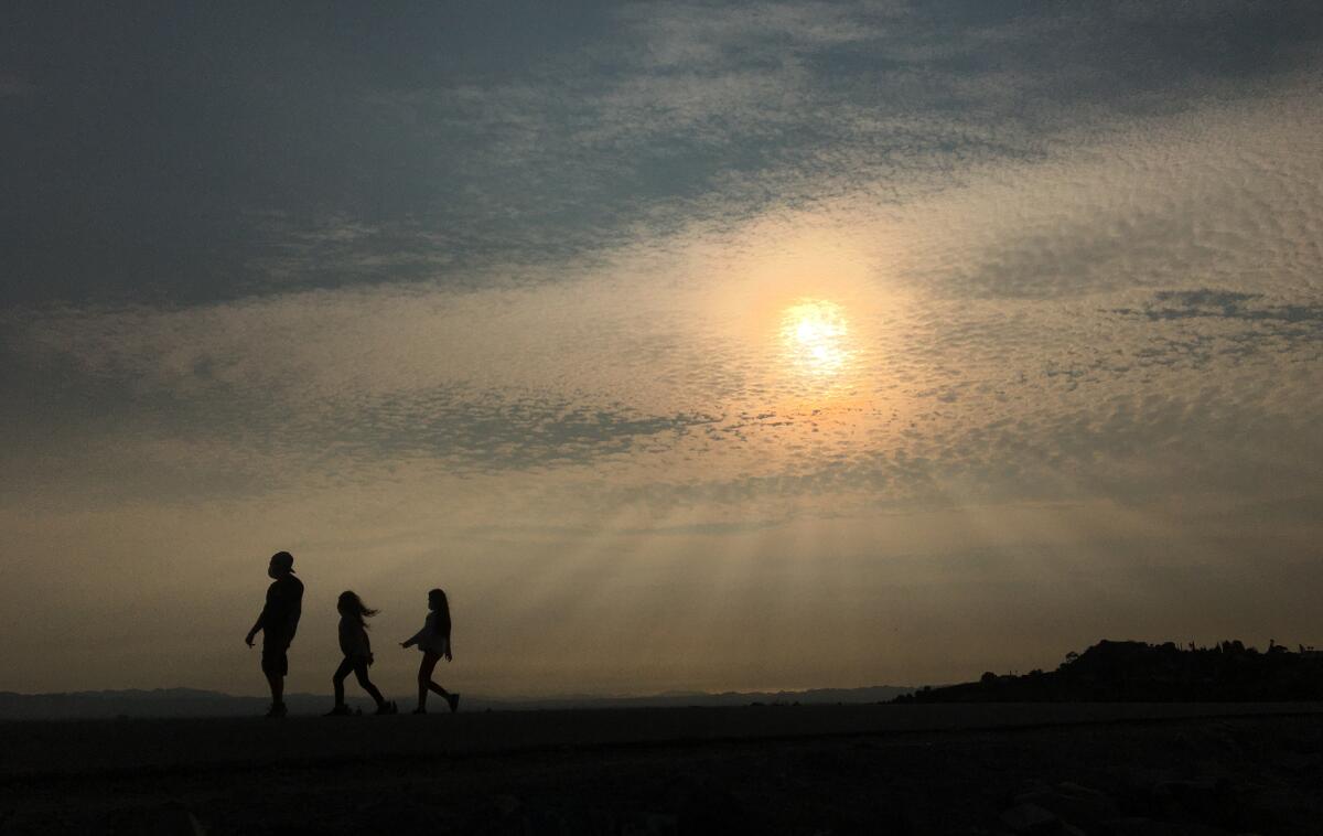 Three people in silhouette are seen walking as sun rays shine through a layer of haze and smoke