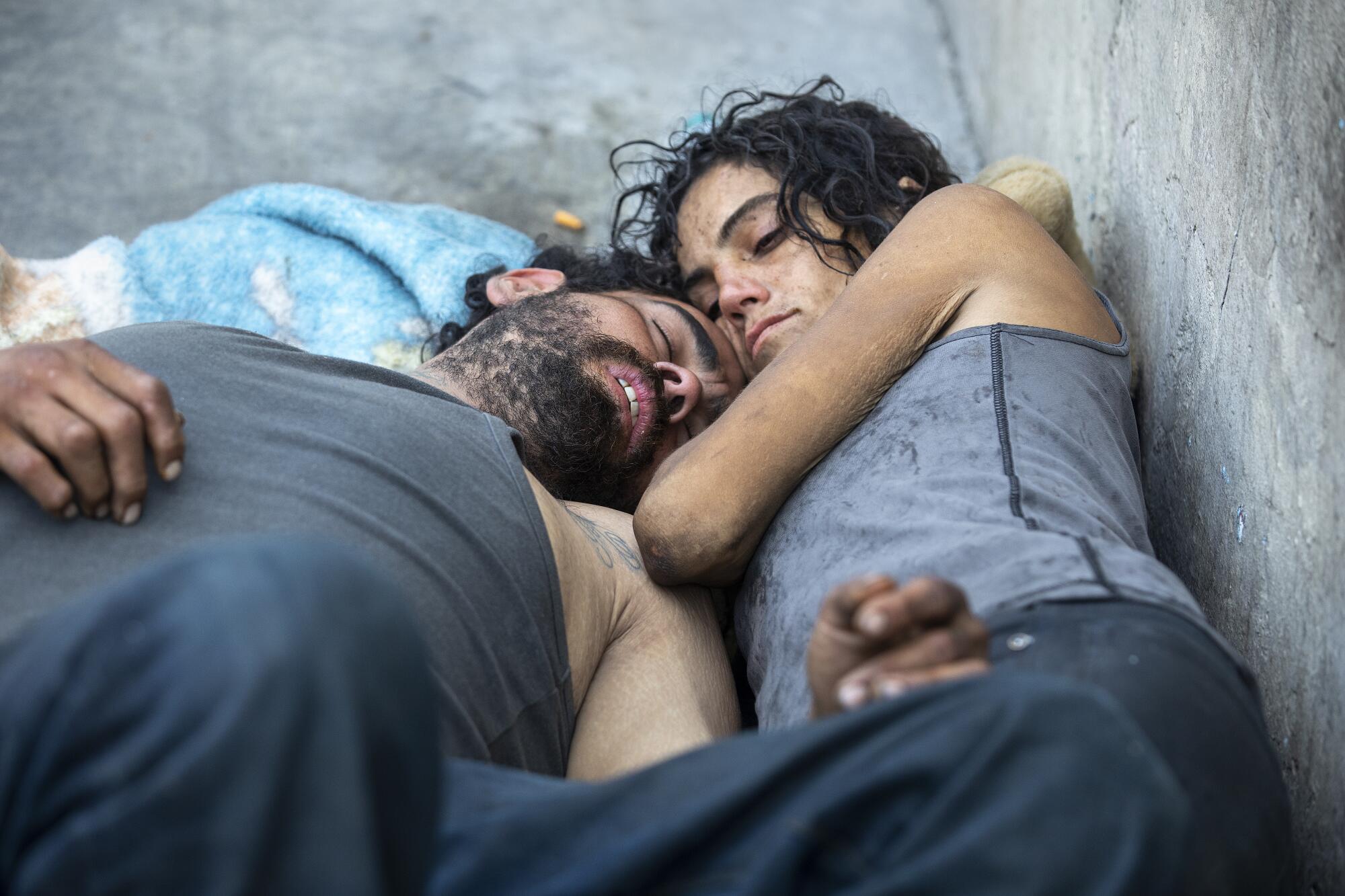 A homeless couple lie down on a blanket on concrete
