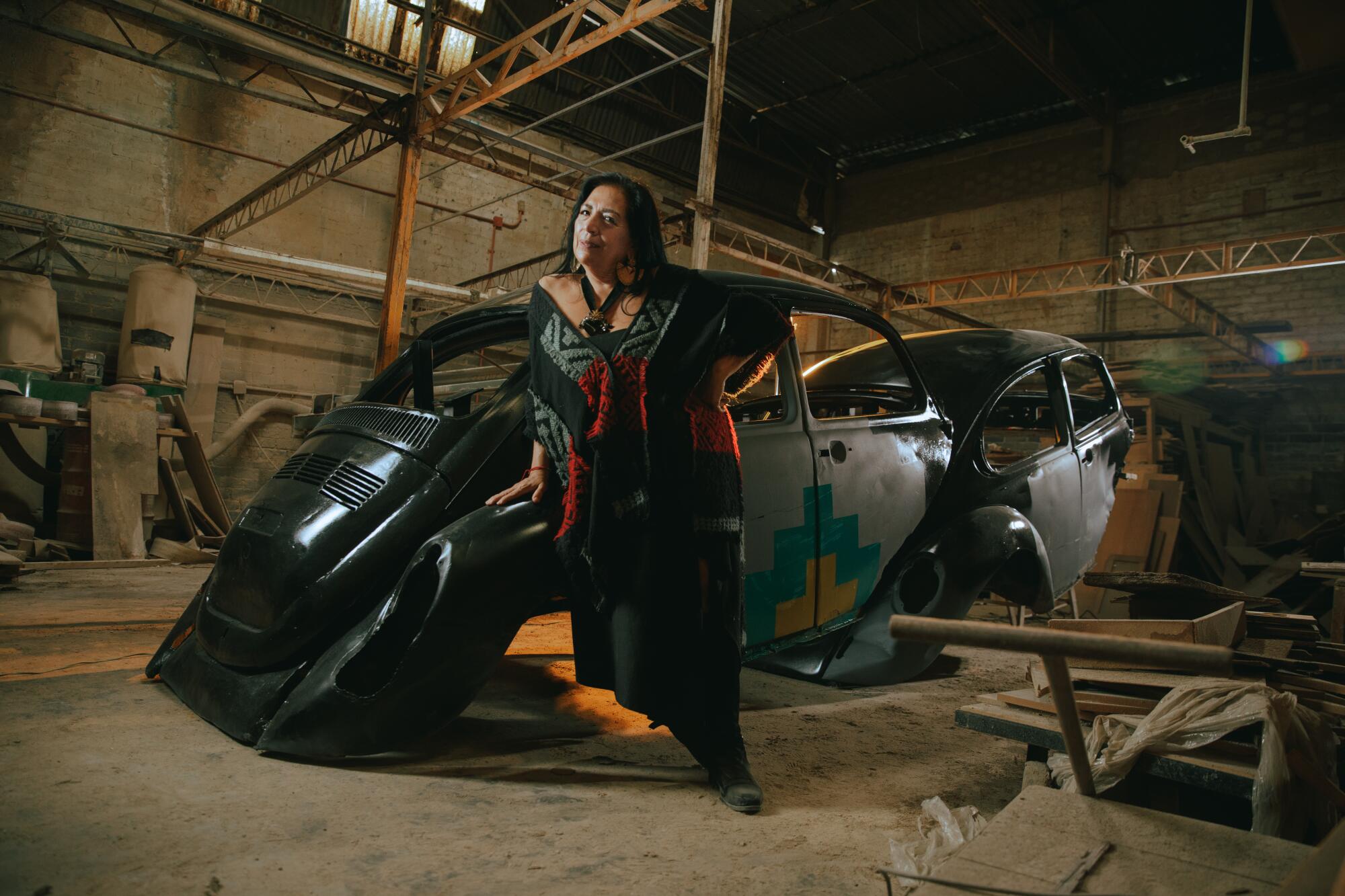 An artist leans against the frame of an old Volkswagen Beetle.