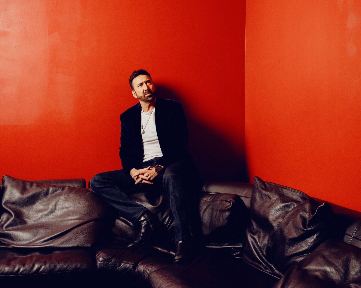 Nicolas Cage sits for a portrait on the top edge of a large couch.