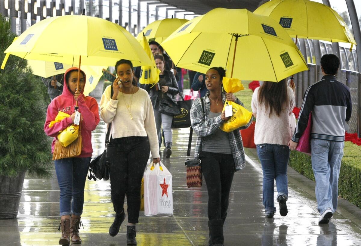 Shoppers armed with borrowed umbrellas and bags of sale items walk through South Coast Plaza on a rainy Black Friday morning.