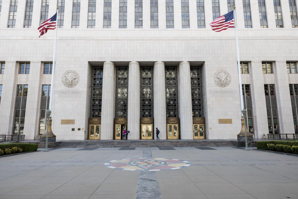 A view of a courthouse with a white facade, official seals and two U.S. flags flying outside