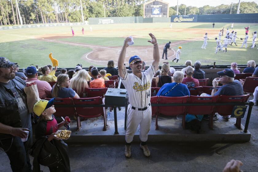 FILE - Savannah Bananas catcher Vinny Rauso, center, tries to get fans to cheer before throwing a free T-shirt to the loudest section, during the team's baseball game against the Florence Flamingos, June 7, 2022, in Savannah, Ga. A new exhibit dedicated to the sport's wackiest team, the Bananas, will open Friday at the Baseball Hall of Fame in Cooperstown, N.Y. (AP Photo/Stephen B. Morton, File)