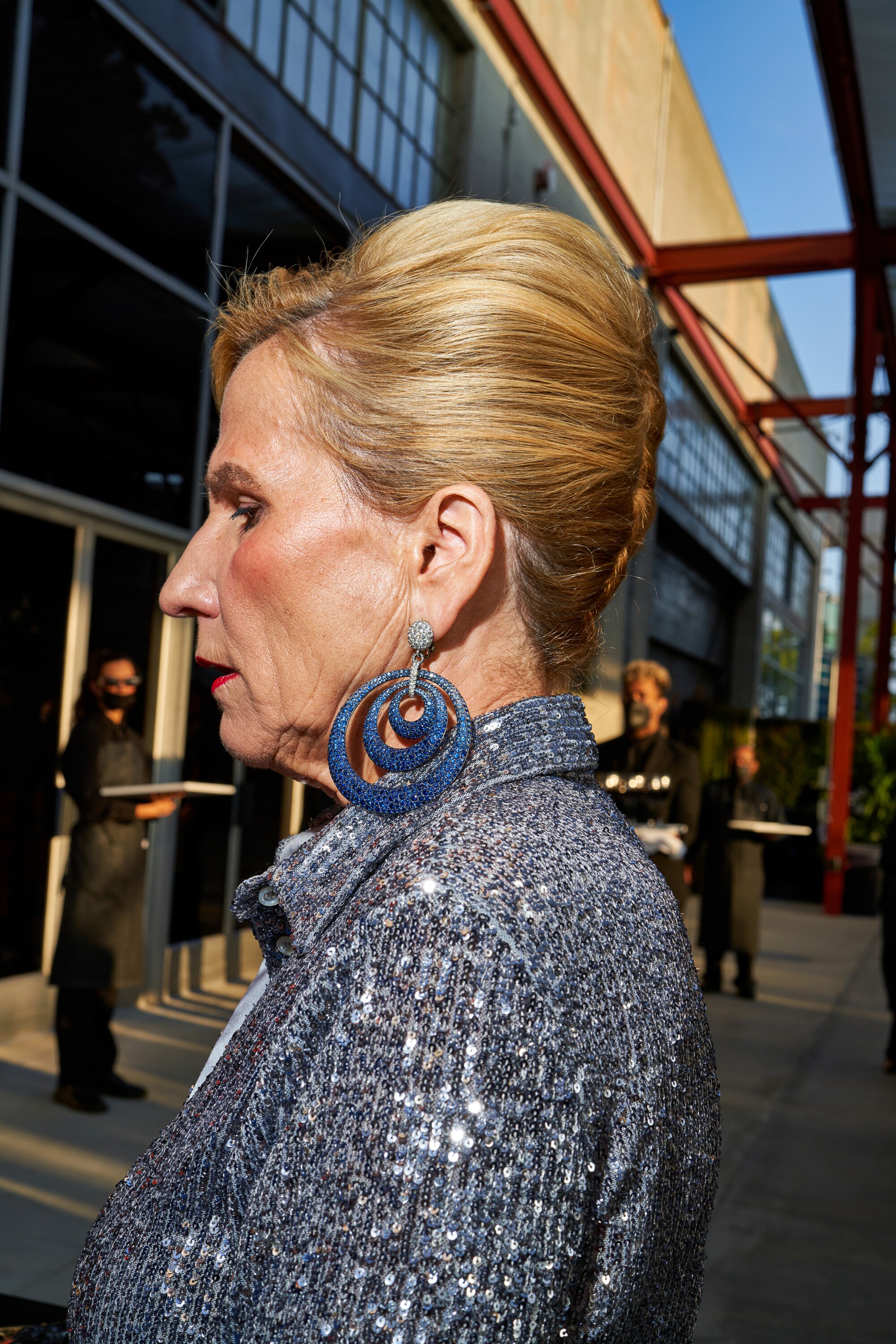 A woman with large blue earrings walks by.