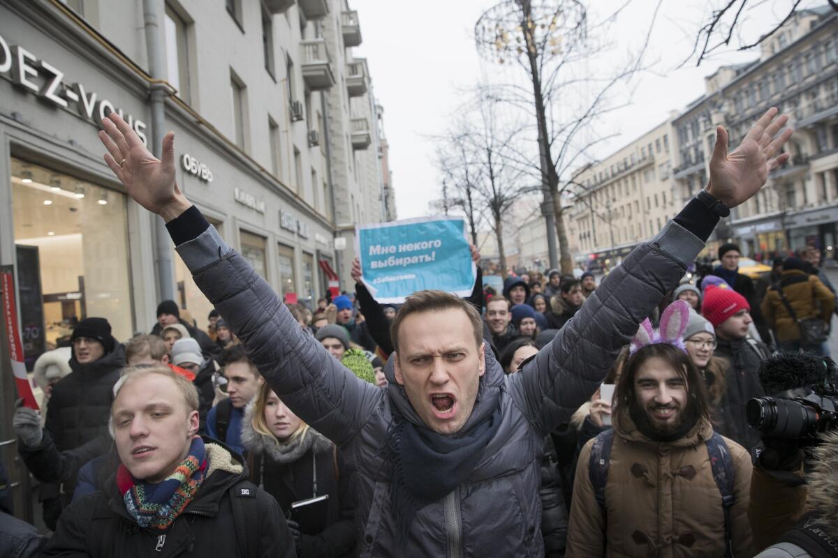 Alexei Navalny, amid marchers in Moscow, raises both arms while surrounded by other people.