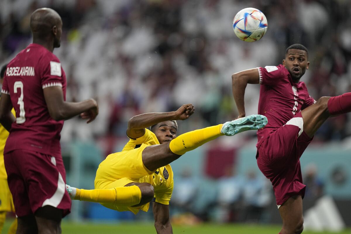 Two soccer players in burgundy uniforms flank a player in yellow who's making a dramatic kick.