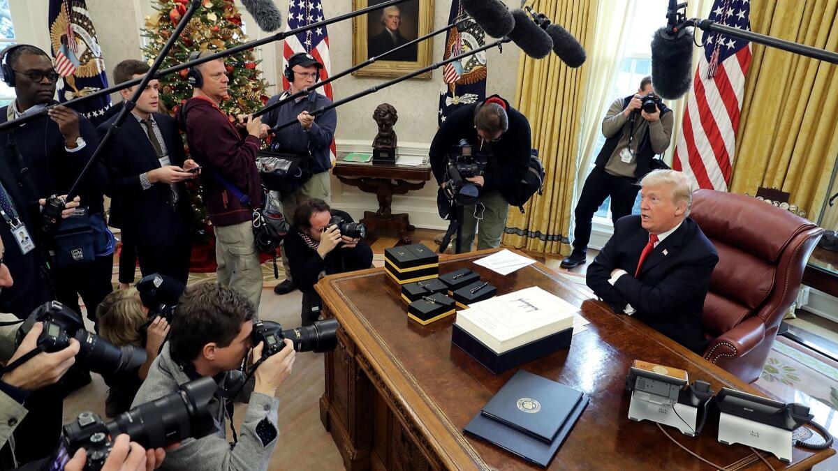 President Trump talks with journalists in the White House Oval Office after signing tax reform legislation in 2017.