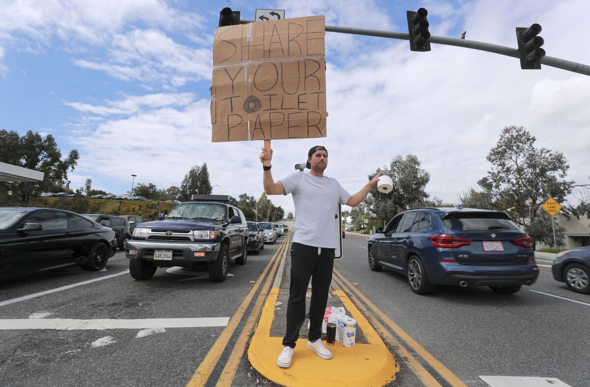 Encinitas resident Jonny Blue, 33, who is a physical therapist, makes a request for toilet paper so that he can in turn give it to drivers that need it while standing at the intersection of Encinitas Boulevard and El Camino Real on March 14, 2020.