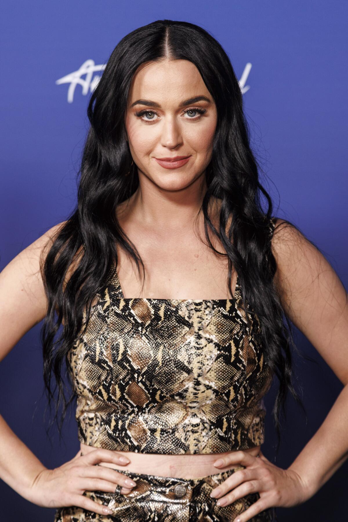 A woman with long, dark hair and a snake-print shirt poses for pictures. 