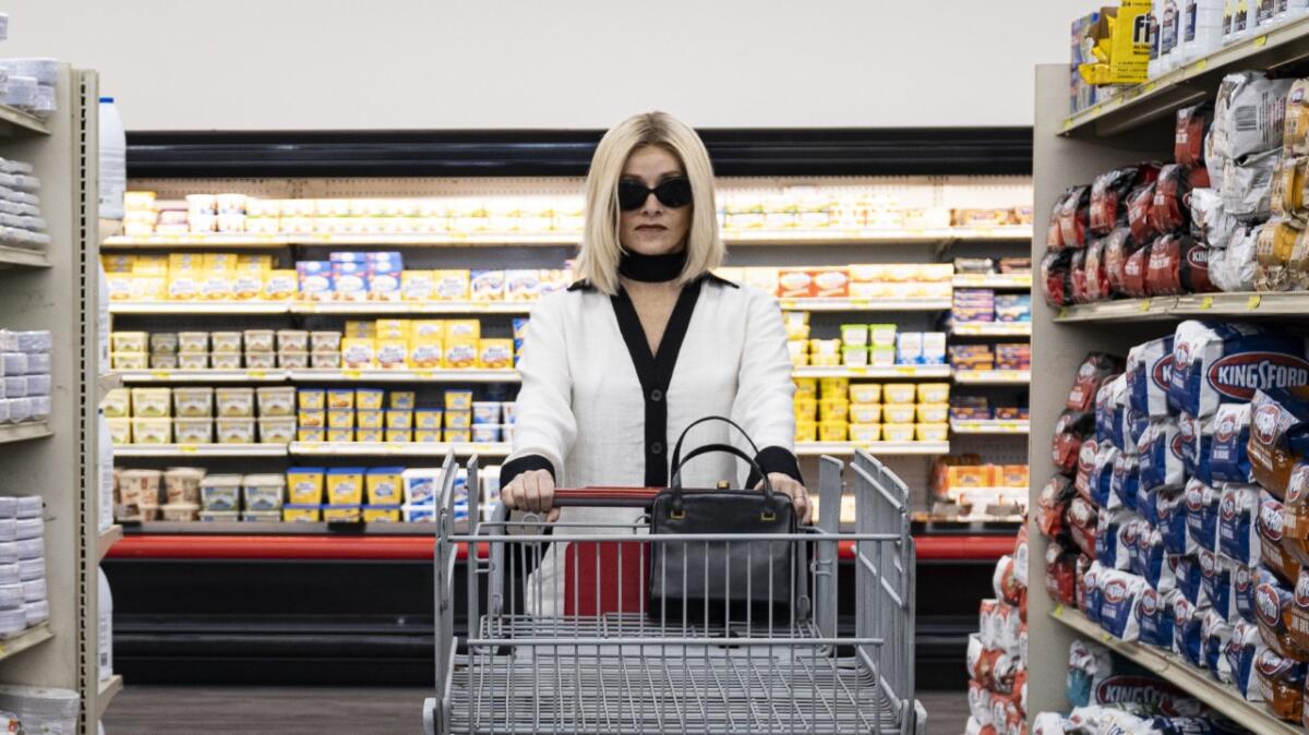 A woman in sunglasses pushing an empty grocery cart down an aisle.