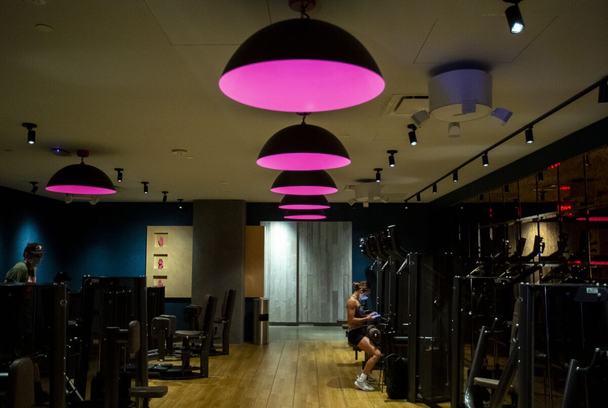 A woman sits at a machine in a gym with purple lights hanging from the ceiling
