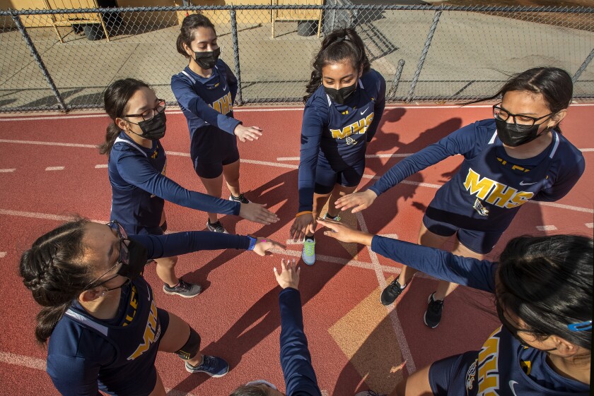 Members of the Montebello High School girls cross country team are careful not to touch hands while wearing masks