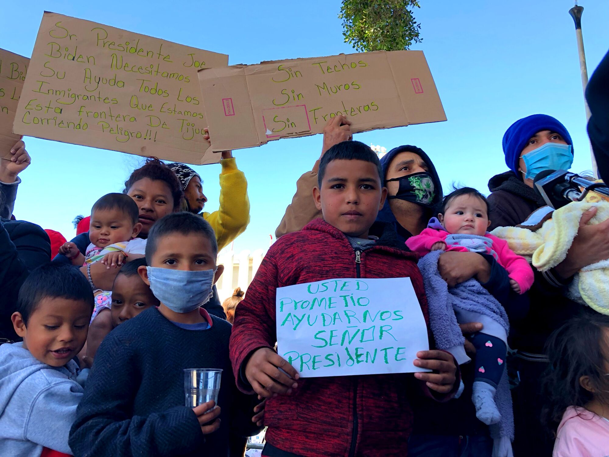 Asylum seekers waiting in Tijuana hold signs asking the United States for help.