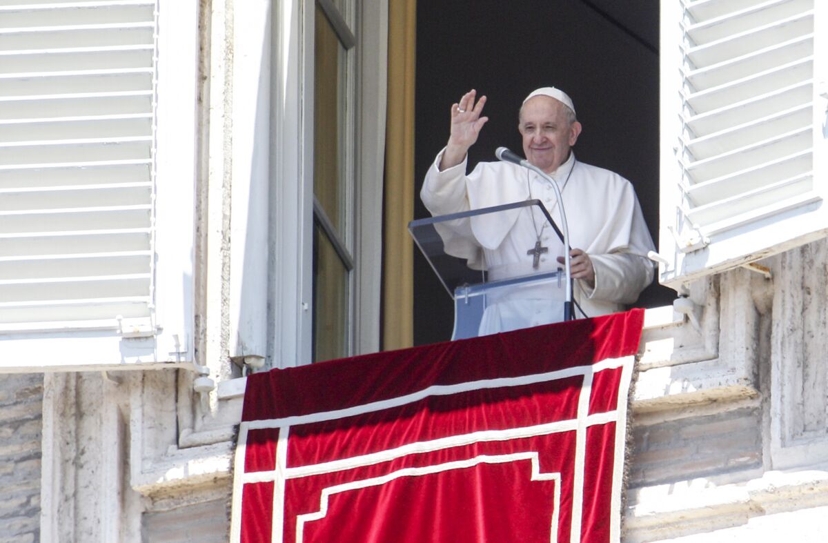 Pope Francis waves from a window with a red banner