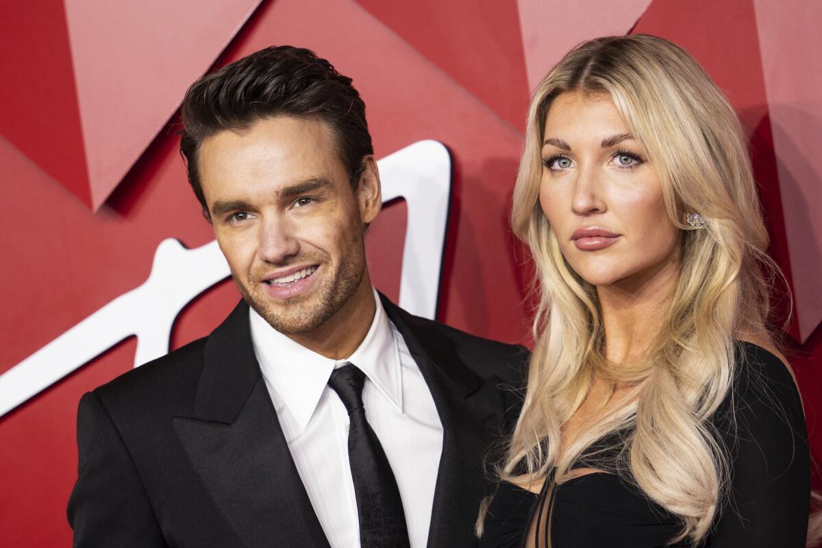 Liam Payne in a suit and Kate Cassidy in black posing at an event