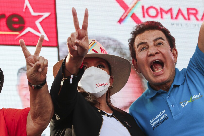 Una mujer enmascarada con sombrero, en el centro, hace el signo de la paz.  Junto a ella hay un hombre con una camisa azul con las palabras Salvador Nasralla.
