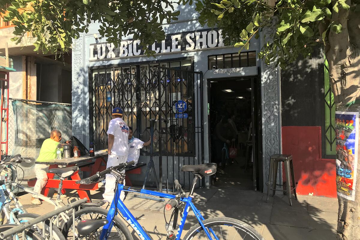The exterior of Lux Bicycle Shop, shaded by trees, with bikes in the rack outside.