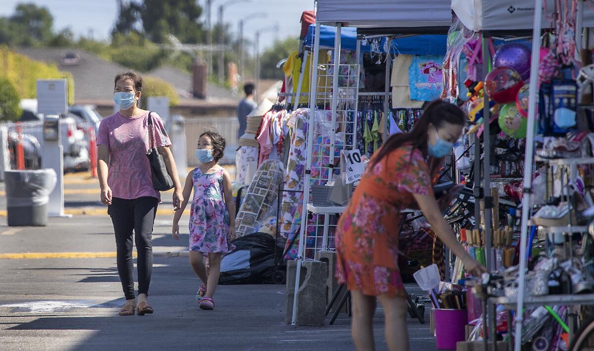 Shoppers in masks walk past stands at an outdoor swap meet