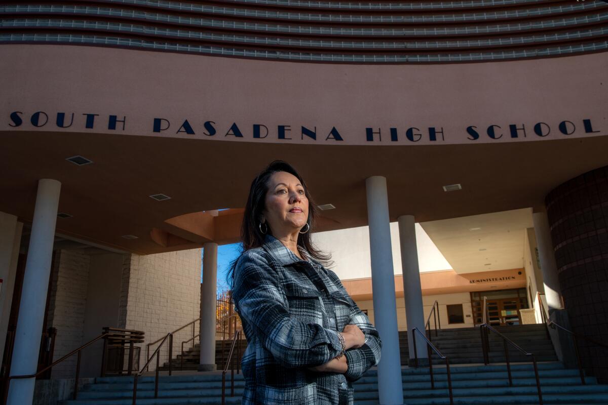 A woman stands in front of a high school. 