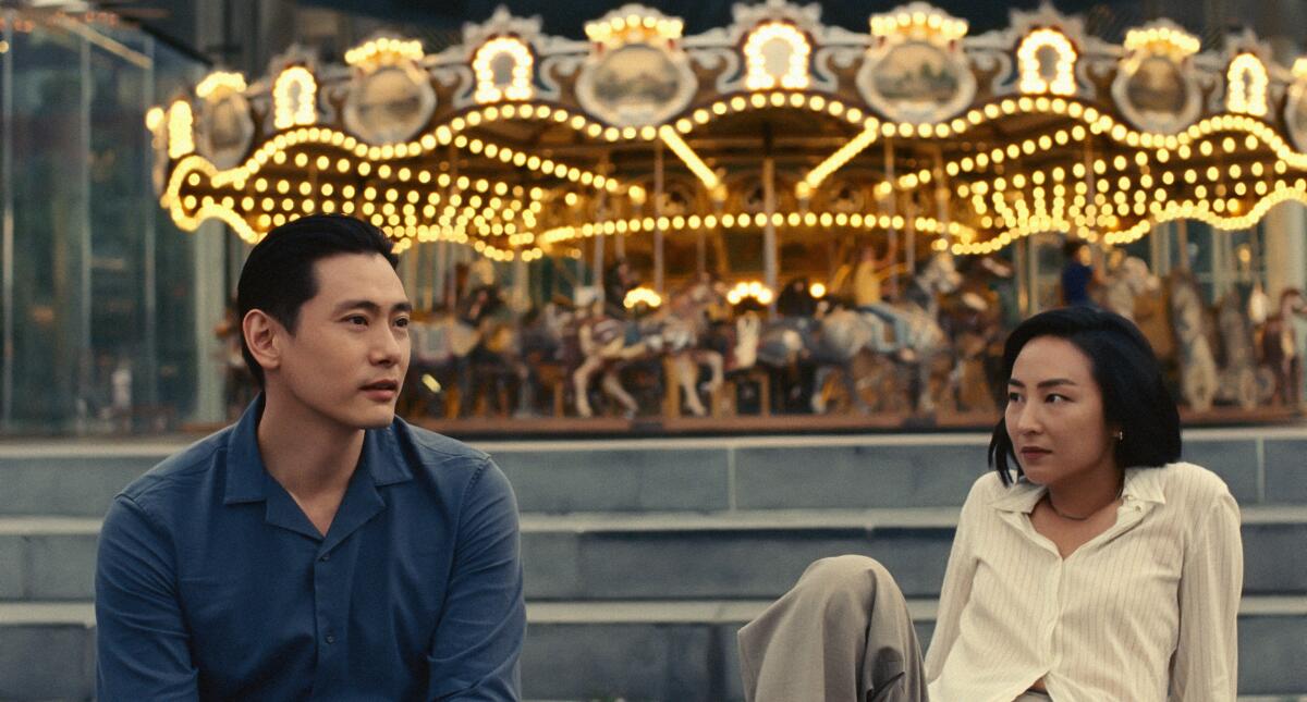A man and woman sit on steps in front of a carousel.