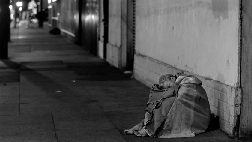 A man sits on a sidewalk in the skid row neighborhood of L.A.