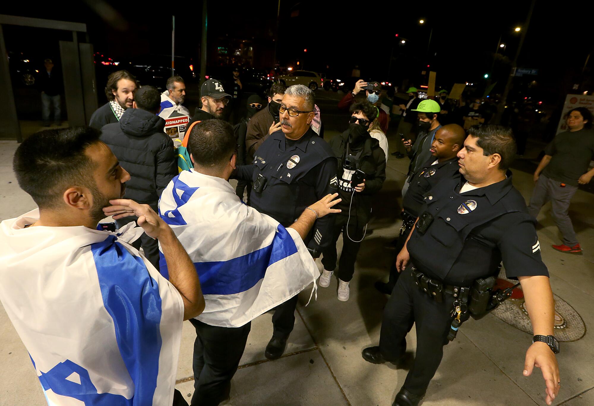 Men draped in Israeli flags stand in front of police officers.