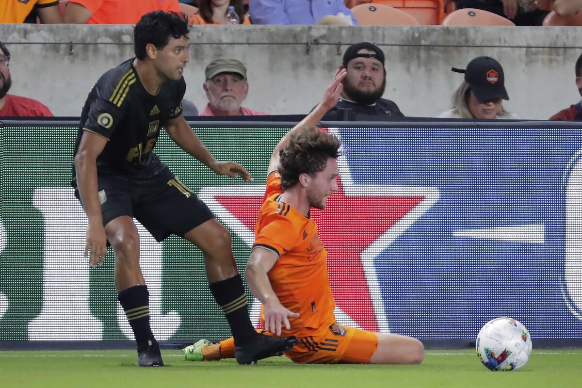 LAFC forward Carlos Vela kicks the ball before a slide tackle by Houston Dynamo defender Adam Lundqvist.