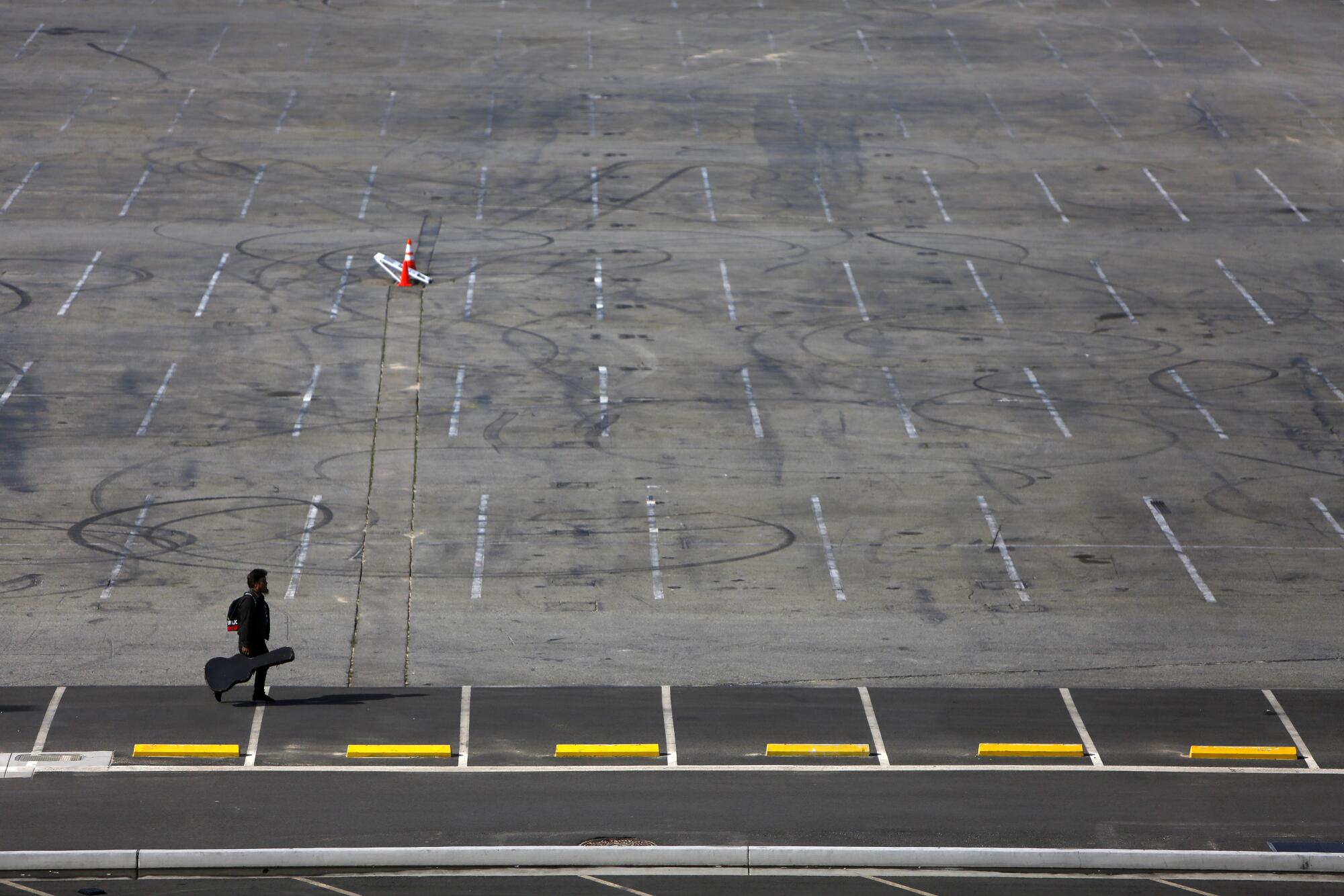 A musician walks across an empty parking lot in Los Angeles.