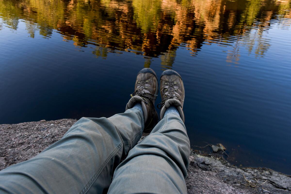 A pair of feet in hiking boots in front of a body of water