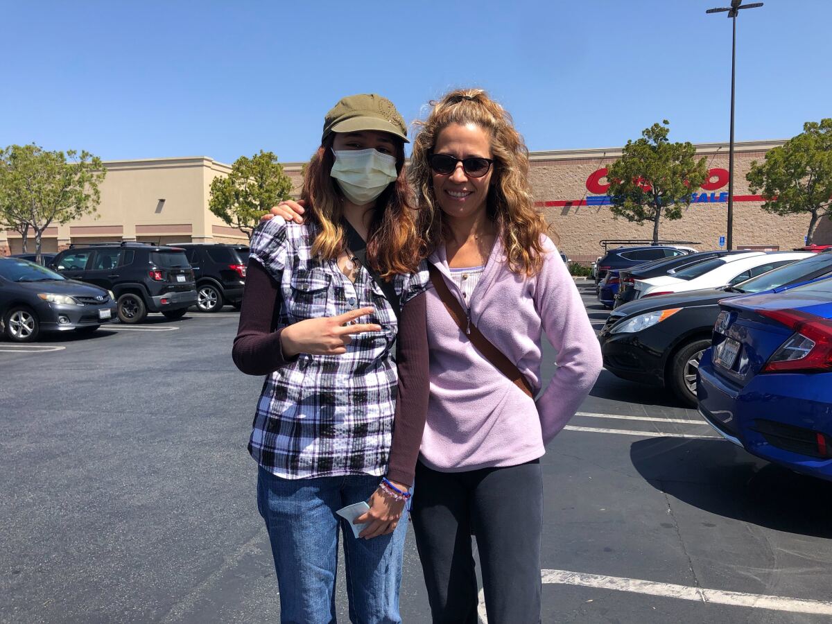 Two women standing in a parking lot, one with her arm around the other.