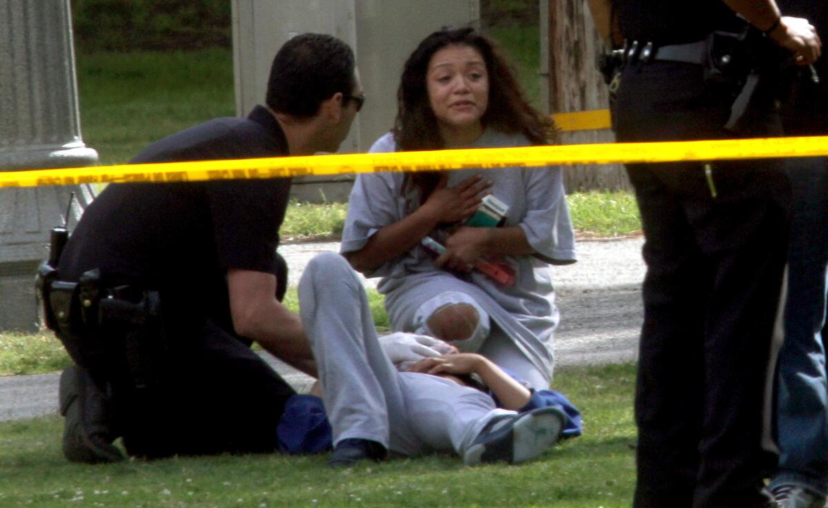 A woman lies on the ground at Point Fermin Park in San Pedro as LAPD officer tends to her wounds and another woman talks to him on May 13.